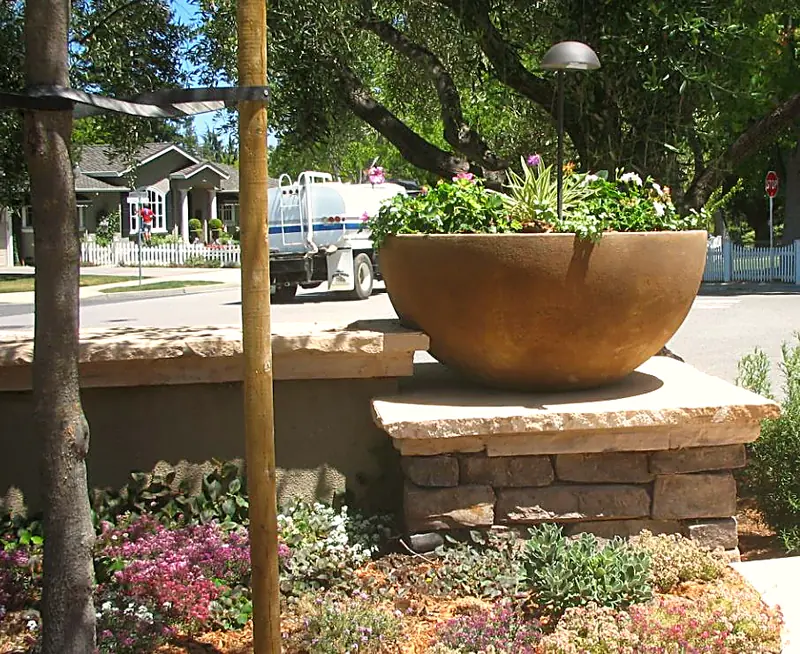 Stone-veneer pilaster with a cast-stone bowl planter, low-voltage lighting, and flowering groundcover — Los Gatos, CA